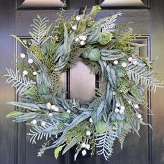 a green wreath with white berries and greenery hangs on a black front door frame