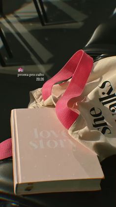 a book with a pink ribbon on top of it sitting next to a white bag