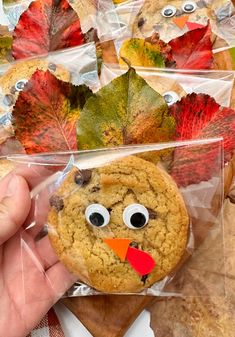 a person holding up a cookie in front of some fall leaves with eyes and nose