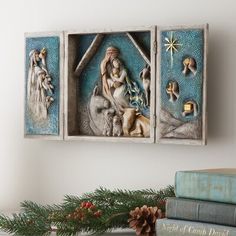 the nativity scene is displayed in three wooden frames on a mantle next to books