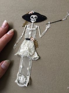 a hand holding a piece of art made to look like a skeleton wearing a hat