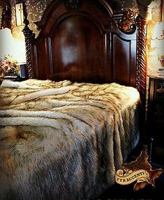 a bed with a fur blanket on top of it next to a night stand and lamp