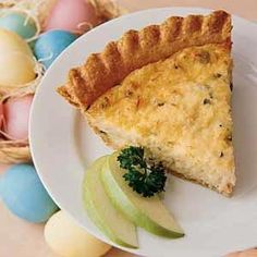 a slice of quiche on a plate with an apple and some eggs in the background