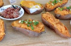 several baked potatoes with different toppings on a cutting board next to bowls of food