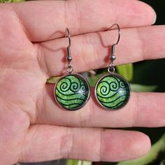 a hand holding a pair of earrings with green swirls on the front and back