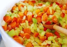 carrots, celery and onions are mixed together in a white bowl with a wooden spoon