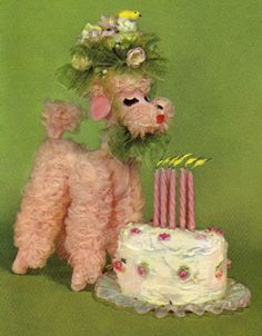 a pink poodle standing next to a cake with candles on it and flowers in its hair