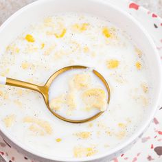 a white bowl filled with cereal and a golden spoon in the middle, on top of a floral table cloth