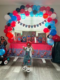 a little boy standing in front of a table with balloons on it and spiderman decorations