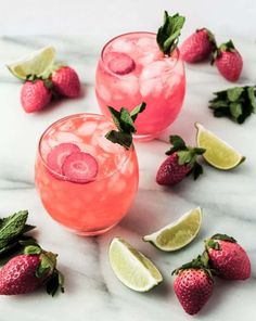 two glasses filled with pink lemonade, lime and mint garnish next to sliced strawberries