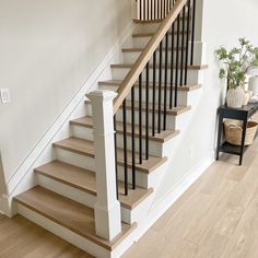 a white staircase with wooden handrails and black railing next to a potted plant