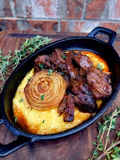 a skillet filled with meat and potatoes on top of a wooden table