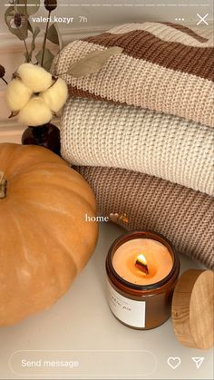 a candle sitting on top of a counter next to some blankets and pumpkins in a vase