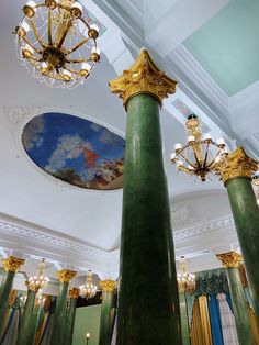 two green pillars in the middle of a room with chandeliers and paintings on the walls