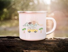 a pink camper mug sitting on top of a wooden table next to a forest