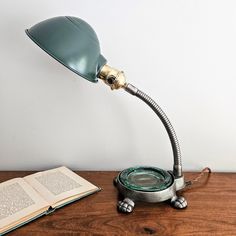 a green desk lamp sitting on top of a wooden table next to an open book