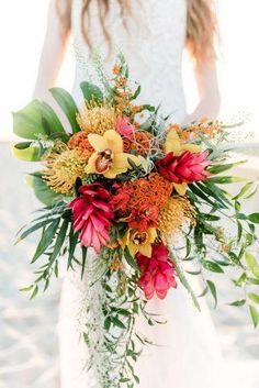 a bride holding a bouquet of flowers in her hands on the beach with sand behind her