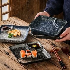 a person holding a black plate with sushi on it