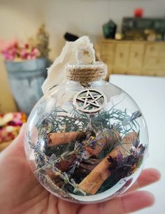 a hand holding a glass ornament filled with herbs and other things in it