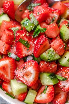 a bowl filled with sliced strawberries and cucumbers