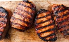 four pieces of meat sitting on top of a wooden cutting board next to each other