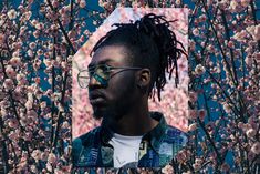 a man with glasses is standing in front of some pink flowers and trees that are blooming