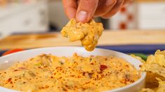 a hand holding a tortilla chip over a bowl of dip and potato chips