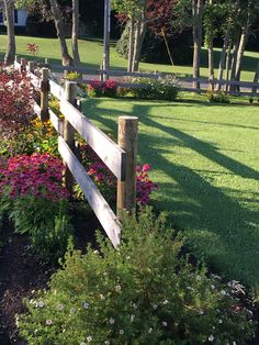 a wooden fence surrounded by flowers and trees in a park with lots of green grass