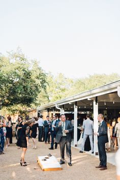 a group of people standing around each other in front of a white building with trees