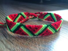 a red, green and yellow braided bracelet on top of a wooden table next to a laptop computer