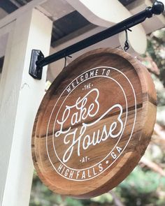 a wooden sign hanging from the side of a white and black building that says lake house at high falls bar