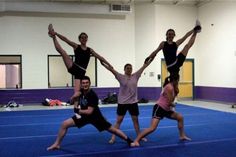 four people doing acrobatic tricks on a blue mat in an indoor gym