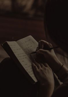 a person writing on a notepad with a pen in their left hand, while sitting down