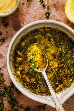 a white bowl filled with soup next to lemon wedges and some herbs on the side