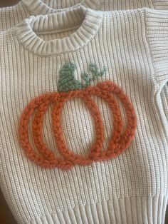 three knitted pumpkins sitting on top of a white sweater with green and orange trim