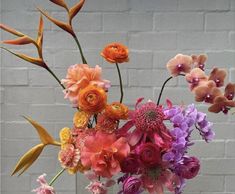 a vase filled with lots of different colored flowers on top of a wooden table next to a brick wall