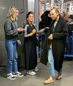 two women standing next to each other in front of a metal structure with people looking at them