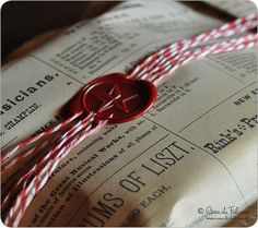 a red wax stamp sitting on top of an open book next to some paper twine