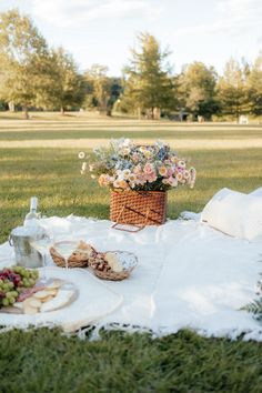 a picnic is set out on the grass with food and flowers in a wicker basket