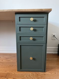 a green cabinet sitting on top of a hard wood floor next to a white wall