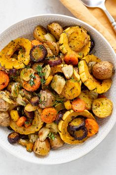 a white bowl filled with roasted vegetables on top of a wooden cutting board next to a fork