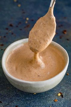 a spoon dipping some kind of sauce in a small white bowl on a blue surface