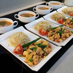 four white plates filled with food on top of a black counter next to cups and saucers