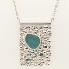 This fun one of a kind Sea Glass and Bubbles Necklace features a frosty chunk of dark aqua sea glass from the coast of California, accented by Sky Blue and London Blue Topaz, all of which are bezel set in fine silver, on a sterling silver bubble-textured background. The pendant rests on an 18" rolo chain that threads through a thick sterling silver tube bail which closes securely at the neck with a lobster claw clasp for your ease of putting it on and taking it off. Measurements: Pendant measure Ocean-inspired Silver Glass Jewelry, Ocean-inspired Silver Necklace With Recycled Glass, Silver Ocean-inspired Necklace With Recycled Glass, Ocean-inspired Silver Glass Necklace, Dark Aqua, Metal Clay Jewelry, Bubble Necklaces, Metal Clay, Rolo Chain