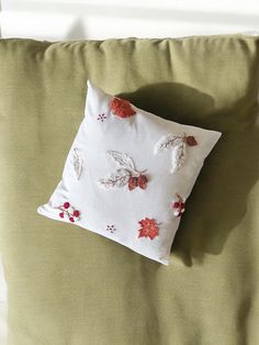 a white pillow with red flowers on it sitting on top of a green bed cover