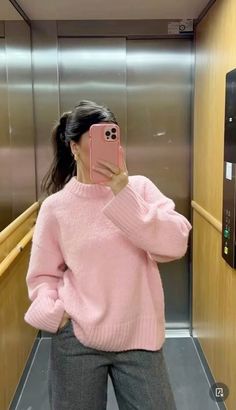 a woman taking a selfie in an elevator wearing a pink sweater and grey pants