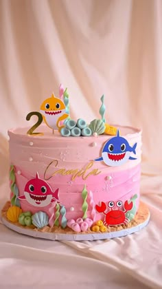 a pink birthday cake decorated with sea animals and under the sea theme, on a white table cloth