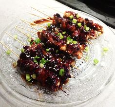 there are skewered meats on the plate with green onions and sesame seeds