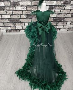 a dress made out of green feathers on a mannequin head stand in front of a brick wall