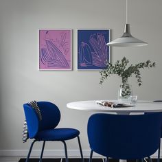 two blue chairs sitting at a white table in front of three paintings on the wall